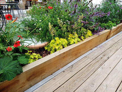 Detail nadzemního záhonu z impregnovaných zahradních pražců a terasy z impregnovaných prken z borovice, oboje Profi impregnace. Detail nadzemního záhonu z impregnovaných zahradních pražců a terasy z impregnovaných prken z borovice, oboje Profi impregnace.