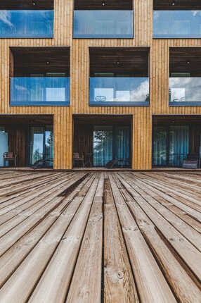 Detail obložení fasády hotelu obkladovými prkny KI Trend. V popředí terasová prkna ošetřena vakuově-tlakovou impregnací. Detail obložení fasády hotelu obkladovými prkny KI Trend. V popředí terasová prkna ošetřena vakuově-tlakovou impregnací.