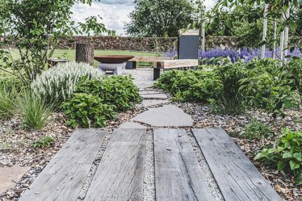 Detail chodníku ze zahradních pražců, v pozadí designové lavičky vyrobeny z pražců a kovových nohou. Zakázková výroba Impregnace Soběslav. Detail chodníku ze zahradních pražců, v pozadí designové lavičky vyrobeny z pražců a kovových nohou. Zakázková výroba Impregnace Soběslav.